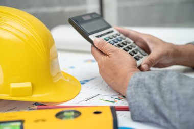 Mimari ev planı projesine sahip Asyalı mühendis şema, grafik ve sarı miğfer ve mühendislik inşaat araçları.