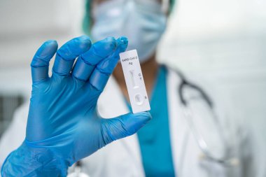 PPE kostümlü Asyalı doktor, Covid-19 Coronavirus 'u kontrol etmek için tükürük Antijen Test kiti ile pozitif sonuç verdi..