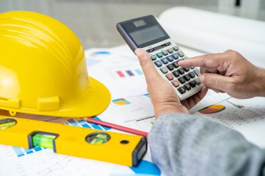 Mimari ev planı projesine sahip Asyalı mühendis şema, grafik ve sarı miğfer ve mühendislik inşaat araçları.