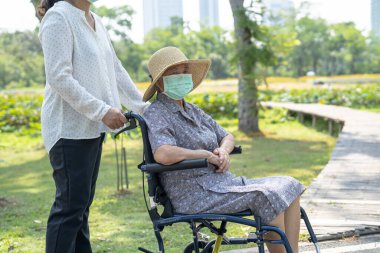 Tekerlekli sandalyedeki yaşlı ve yaşlı kadına yardım edin ve parktaki Covid-19 Coronavirus 'u korumak için maske takın..