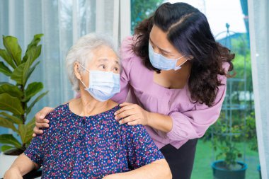 Bakıcı, Asyalı yaşlı ya da yaşlı kadın tekerlekli sandalyede oturan ve güvenlik enfeksiyonunu korumak için maske takan Covid19 Coronavirus 'a yardım ediyor..