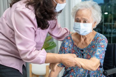Bakıcı, Asyalı yaşlı ya da yaşlı kadın tekerlekli sandalyede oturan ve güvenlik enfeksiyonunu korumak için maske takan Covid 19 Coronavirus 'a yardım ediyor..