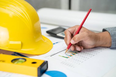 Planlı proje planı, grafik ve sarı miğfer ve mühendislik araçlarına sahip Asyalı mühendis.