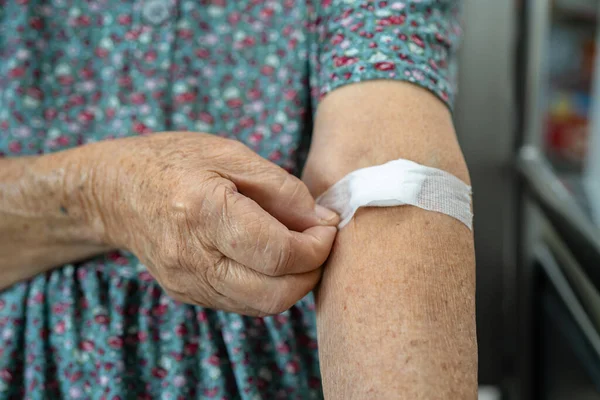 Asian senior or elderly old lady woman patient show cotton wool stop bleeding, after blood drawing testing for annually physical health check up to check cholesterol, blood pressure, and sugar level.