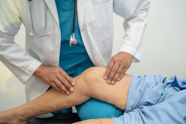 Ortopedi kliniğinde kıdemli bir hastanın diz ve bacağını muayene eden Asyalı doktor fizyoterapisti..