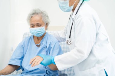 Doktor, güvenlik enfeksiyonunu korumak ve Covid-19 Coronavirus 'u öldürmek için hastanede maske takan yaşlı ve yaşlı bir kadına yardım ediyor..