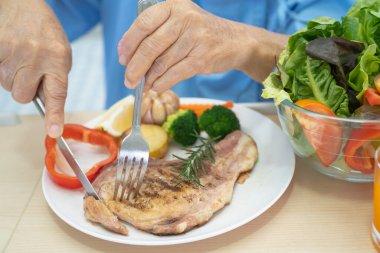 Asyalı yaşlı ya da yaşlı kadın hasta kahvaltı ve sebze yiyen umut dolu ve mutlu bir şekilde hastanede aç bir şekilde yatarken sağlıklı yiyecekler yiyor..