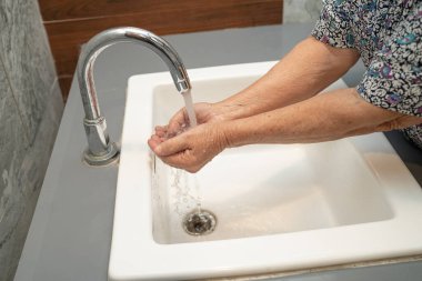 Güvenli enfeksiyonu korumak ve Coronavirus Covid19 virüsünü, bakterileri ve mikropları öldürmek için sabun ve temiz suyla elini yıkayan yaşlı, Asyalı yaşlı kadın hasta..