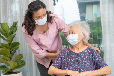 Bakıcı, Asyalı yaşlı ya da yaşlı kadın tekerlekli sandalyede oturan ve güvenlik enfeksiyonunu korumak için maske takan Covid19 Coronavirus 'a yardım ediyor..