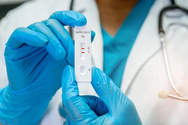 Asian doctor in PPE suit show positive test result with Saliva Antigen Test Kit for check Covid-19 coronavirus in hospital.