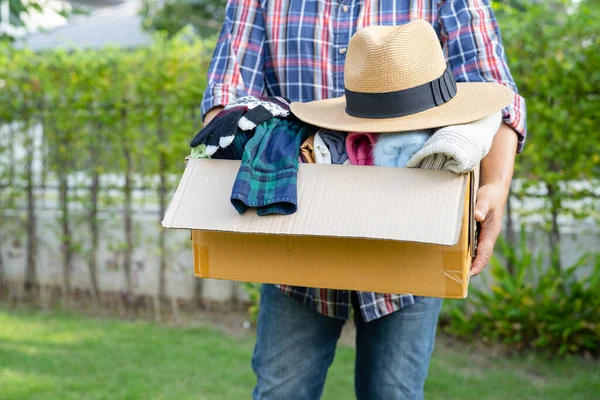 Holding clothing donation box with used clothes and hatl at home to support help for poor people in the world.