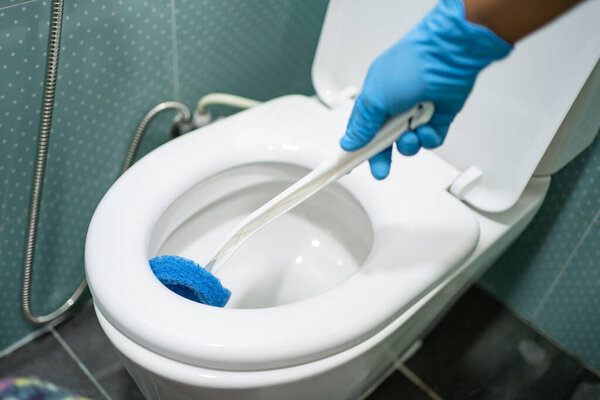Maid cleaning toilet bowl with brush in bathroom at home.