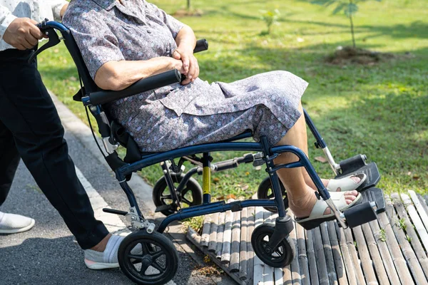 Caregiver help and care Asian senior or elderly old lady woman patient sitting on wheelchair in park, healthy strong medical concept.