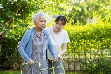 Caregiver help and care Asian senior or elderly old lady woman use walker with strong health while walking at park in happy fresh holiday.