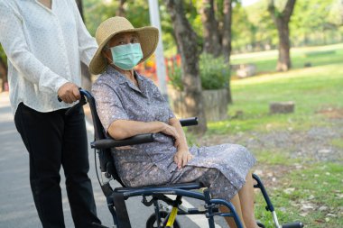 Tekerlekli sandalyedeki yaşlı ve yaşlı kadına yardım edin ve güvenlik enfeksiyonunu korumak için maske takın. Parkta Covid19 Coronavirus.