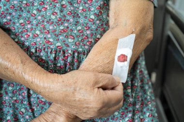 Asyalı yaşlı ya da yaşlı kadın hasta pamuk kanamasının durduğunu gösteriyor. Kolesterol, kan basıncı ve şeker seviyesini kontrol etmek için her yıl yapılan kan tahlillerinden sonra..