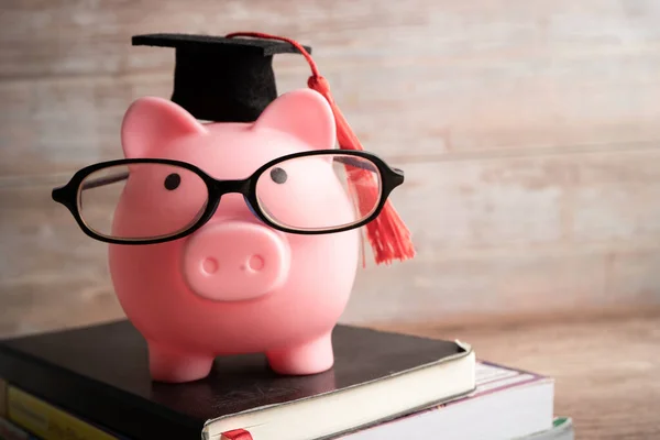 Pigging bank wearing eyeglass and graduation hat on book; education concept.