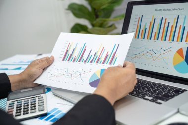 Modern ofis, finans ve iş konseptinde grafik grafik grafiği ve hesap makinesiyle çalışan ve finansal raporları analiz eden Asyalı muhasebeci.