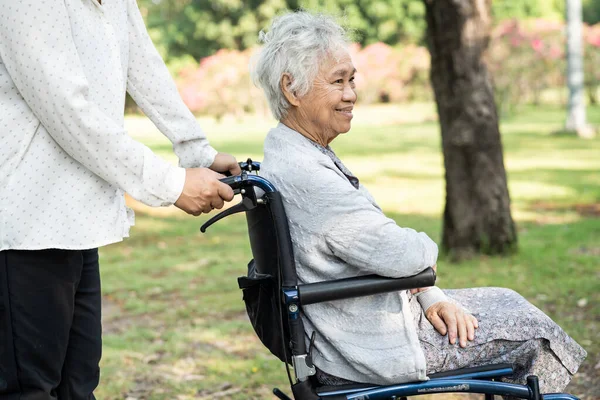 Caregiver help and care Asian senior or elderly old lady woman patient sitting and happy on wheelchair in park, healthy strong medical concept.