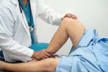 Ortopedi kliniğinde kıdemli bir hastanın diz ve bacağını muayene eden Asyalı doktor fizyoterapisti..