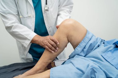 Ortopedi kliniğinde kıdemli bir hastanın diz ve bacağını muayene eden Asyalı doktor fizyoterapisti..