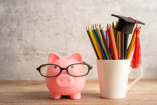 Pigging bank wearing eyeglass with colorful pencils; saving bank education concept.