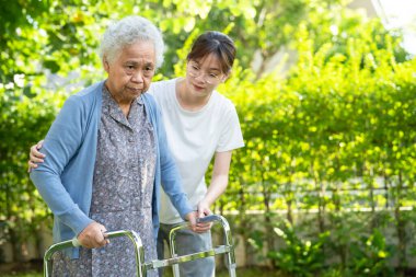 Caregiver help and care Asian senior or elderly old lady woman use walker with strong health while walking at park in happy fresh holiday.