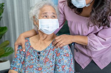 Bakıcı, Asyalı yaşlı ya da yaşlı kadın tekerlekli sandalyede oturan ve güvenlik enfeksiyonunu korumak için maske takan Covid 19 Coronavirus 'a yardım ediyor..