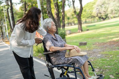 Bakıcı yardım ve bakım Asyalı yaşlı ya da yaşlı kadın hasta parkta tekerlekli sandalyede oturuyor ve mutlu, sağlıklı güçlü tıbbi konsept..
