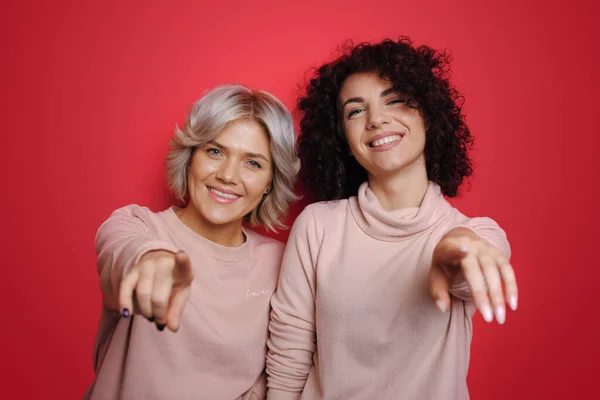 Schönheit Gesicht. Modemodell. Lockenhaarige Frauen zeigen in die Kamera. Einladungsgeste für Sie. Blond und brünette schwester. — Stockfoto