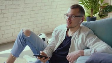 Gözlüklü bir adamın bluetooth 'la hava podlarına telefon bağlayıp yerde oturduğu bir video. Mobil iletişim