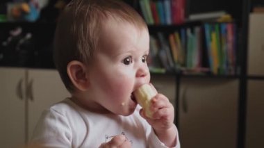 Elinde muz tutan ve küçük ağzıyla ısıran bir bebeğin videosu. Bebek alkışları. Komik mutlu bebek. Yavrum. Aktif sağlıklı çocukluk.
