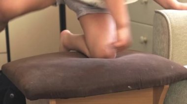 Video kaydı. Aktif çocuk sandalyeye tırmandı ve sonra koltuğa oturdu, karnının üzerinde sandalyede yatıyordu. Etkin çocukluk