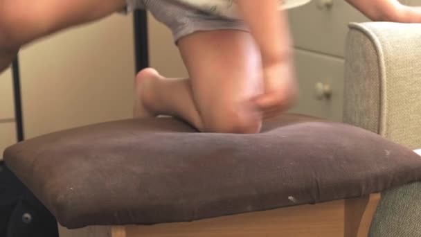 视频。活泼的男孩爬上了椅子，然后躺在沙发上，趴在椅子上。活跃的童年 — 图库视频影像