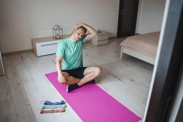 男子双腿交叉坐在健身床垫上，暖脖子肌肉进行晨练。保健服务 — 图库照片