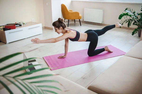 Mujer deportiva haciendo entrenamientos en línea aislados en casa, sosteniendo la mano izquierda extendida hacia adelante y la pierna derecha levantada. Mujer calentando la pierna, gran diseño para cualquier — Foto de Stock