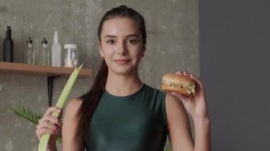 Elinde bir hamburger ve soğanla kameraya bakan sportif bir kadının videosu. Sağlıklı beslenme