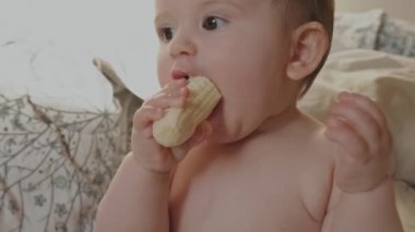 Şevkle muz yiyen bir bebeğin videosu, ona bakıyor. Sağlıklı yemek. Sağlıklı yiyecekler. Komik mutlu bebek.