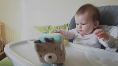 Bebeğin annesinin eliyle beslendiği bir video. Özel bir sandalyede çocuk masası yemek yemeyi reddediyor ve sarı plastik oyuncağı ağzına koyuyor.