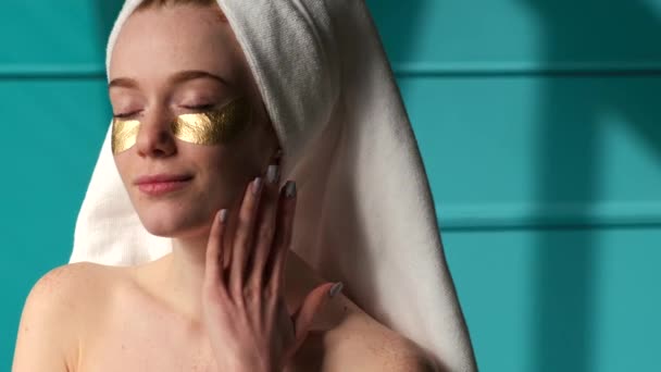 Video s pihovatou ženou, jak vychází ze sprchy s bílým ručníkem na hlavě. Smyslně se dotýká jeho tváře a krku na modrém pozadí — Stock video