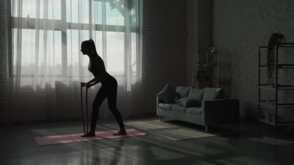 Video van een silhouet van een vrouw die traint met de verzetsband in haar kamer. Gezonde levensstijl — Stockvideo