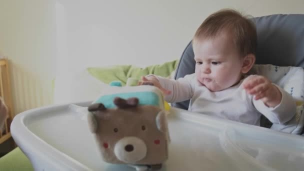 Vídeo com um bebê sendo alimentado pela mão das mães. Mesa infantil em uma cadeira especial recusa comida e coloca o brinquedo de borracha amarela em sua boca — Vídeo de Stock