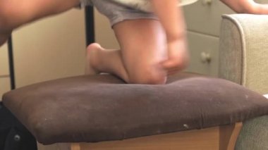 Video kaydı. Aktif çocuk sandalyeye tırmandı ve sonra koltuğa oturdu, karnının üzerinde sandalyede yatıyordu. Etkin çocukluk