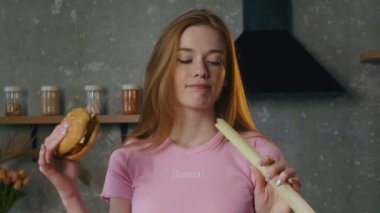 Sağ elinde hamburger, sol elinde soğan tutan bir kadının neyi seçeceğini düşünürken çekilmiş videosu. Soğanı tadıyordu, iğrenmişti.