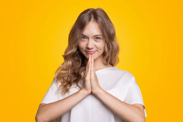 Junge Europäerin auf gelbem Hintergrund mit blonden und welligen Haaren. Porträt einer Frau, die lächelt und ihre Hände in einer Gebetsposition hält — Stockfoto