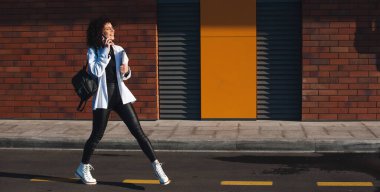 Şehrin sokaklarında yürüyen bir kadın telefonda konuşuyor. Elinde dizüstü bilgisayar ve tablet olan bir öğrencinin görüntüsü. Tuğla duvar Güneşli bir gün