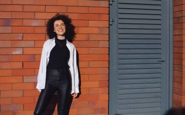 Tuğla duvarda poz veren genç kıvırcık kadın. Her tasarım için boş yer