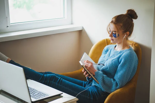 Mujer tomando notas mientras participa en clases en línea sentado relajado en el sillón. Trabajo independiente. — Foto de Stock