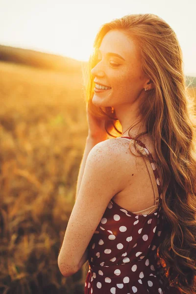 Vista dal lato di una giovane donna che sorride nel campo di grano. Viso e spalle macchiati. Tramonto nel campo di grano — Foto Stock