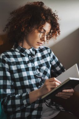 Kıvırcık kadın defterine bir şey not ediyor. Günü planlıyorum. Ev izolasyonu